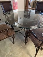 View of round glass table top and two chairs showcasing metal and wooden frame design and upholstery