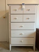 Front view of the white dresser showing five drawers with round white knobs.