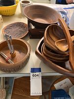 Photo showing large teak bowl, stacked smaller wooden bowls, wooden utensils, nut holder with nutcrackers, and other wooden serving pieces arranged on table.