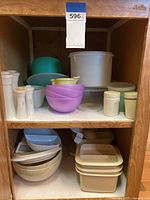 Front view of multiple Tupperware items and microwavable cookware arranged on two shelves showing bowls, containers with lids, and salt and pepper shakers.