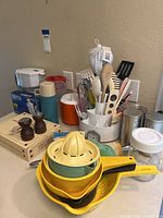 Photo of the kitchenware including utensil carousel with kitchen utensils, yellow juicers, blue thermos, and wooden salt and pepper grinders.