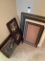 Group of seven vintage picture frames and framed art pieces leaning against a wall, including frames with artworks and empty frames.