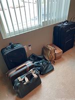 Photo showing several pieces of luggage on floor near a window, including hard and soft styles.
