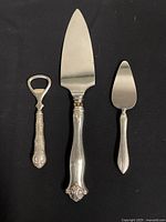 All three items on black background showing pie cutter, cheese cutter, and bottle opener with detailed sterling silver handles.