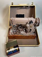 Full view of Singer 306K sewing machine inside its hard-shell carrying case with a small opened tin of accessories in front.