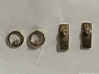 Two pairs of gold diamond stud earrings on white background, one circular pair and one rectangular band pair each with small diamond in center.