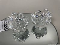 Two Swarovski crystal bird's nest figurines on a faceted mirrored base and one separately.