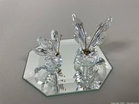 Two Swarovski crystal butterfly figurines on an octagonal mirror base showing their size and reflections.