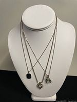 Three sterling silver necklaces displayed on white bust showing presence of minor tarnishing and detailing on pendants.