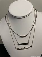 Three layered 925 silver necklaces displayed on a white bust, showing a curved bar pendant, a rectangular engraved bar pendant, and a cursive name pendant 'Anastasio'.