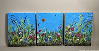 Full view of three connected oil paintings forming a triptych with wildflower and grass scene on bright blue background.