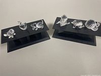 Six Swarovski crystal animal figurines displayed on two black stands, including a duck, turtle, snail, and other small animals.