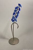 Full view of sapphire-blue crystal flower sculpture on silver-tone metal stand against white background