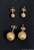 Both pairs of ball stud earrings laid out on black fabric