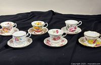 Three bone china teacup and saucer sets with various floral patterns displayed on black cloth.