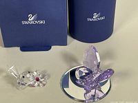 Violet crystal butterfly and clear baby bird with flower Swarovski figurines alongside original blue Swarovski boxes.