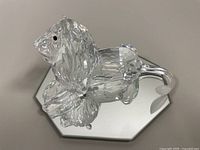 Top and side view of the clear faceted crystal lion on octagonal mirrored base, showing full body and facial details.