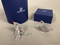 Both crystal figurines side by side with their original blue Swarovski boxes visible behind them.