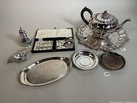 Photo showing the full assortment of silver plated items including teapot, sugar shaker, trays, and spoon set