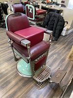 Front-left three-quarter view of barber chair showing mint green base, burgundy vinyl upholstery and footrest