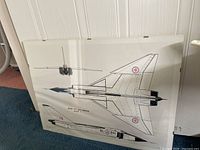 Framed mounted drawing of Avro CF-105 Arrow Mark 1 aircraft displayed on the floor, showing top and side views with detailed design and markings.