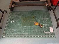 Photo of large green Hobbico builders cutting mat with grid lines on floor between two metal stands.