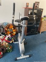 Front view of manual exercise bike showing adjustable seat, black handlebars, and silver frame.