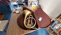 Vintage brass French horn inside the maroon-lined fitted case, showing coiled tubing and rotary valves.