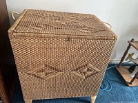 View of rectangular wicker laundry hamper with woven pattern, side rope handles visible