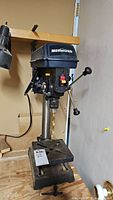 Front view of Mastercraft drill press showing drill bit, base, and control panel.