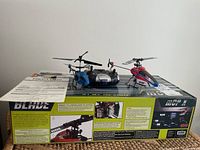 Two Blade Neptune 2.5 channel infrared helicopters in blue and red on the product box alongside an instruction manual.