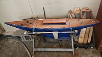 Wooden sailboat hull strapped to metal stand in garage