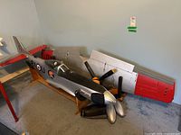 Overview of silver and red P51 Mustang fuselage on wood stands with detached wings and propellers arranged behind it.