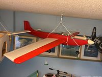Red RC aircraft suspended by cords showing right side profile with visible engine and landing gear.
