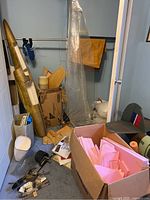 Closet view showing two metallic gold fuselage halves, wooden mould panels, box of pink foam sheets and loose hardware on floor