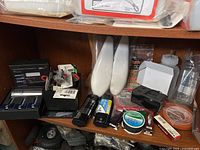 Shelf with assorted RC parts including two sets of rechargeable batteries, white plastic covers, small electronic components, and a boxed pneumatik retract landing gear set