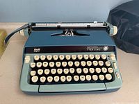Front view of the Smith-Corona Sterling manual typewriter showing blue body, cream round keys with letters and numbers, carriage return lever and platen knob on right.