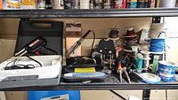 Overview of the workspace with soldering irons, wires, and accessories on shelving.