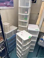 Multiple plastic storage drawer cabinets grouped together in basement room, showing various sizes and drawer counts.