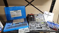 Mastercraft 60-piece tap and die set and PowerFist 39-piece tap and die set open to show all tools organized inside their respective cases with instruction manuals.