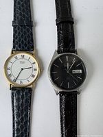 Photo of two vintage Seiko men's quartz watches side by side, one gold-tone with white dial, one silver-tone with black dial.
