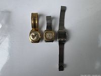 Three vintage men's watches arranged side by side on white background. Left: gold-tone Timex, middle: silver-tone Timex, right: silver-tone digital watch.