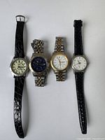 Four vintage men's watches laid flat showing all watch faces and bands, displaying condition and variety of styles including leather and metal bands.