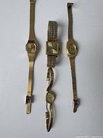 Four vintage women's watches with varying metal bands and face shapes laid out on a white surface.