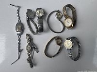 Full lot view of eight vintage women's watches in various styles and conditions, arranged on a white surface.