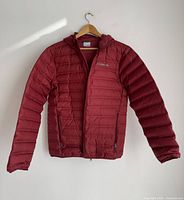 Full front view of the red insulated Columbia jacket with hood, displayed on a hanger against a white wall.