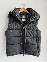Front view of black men's puffer vest with hood hanging on a wooden hanger