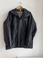 Front view of black Patagonia jacket on hanger showing full front zipper, adjustable hood, and long sleeves.