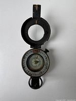 Top view of the opened compass showing the dial and needle, with a partially worn paint on the black metal casing.