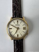 Close-up view of Bulova Accutron watch face showing gold-tone case, silver dial, date window, and leather strap pattern.